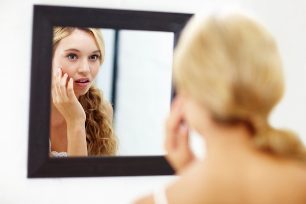 Woman looking at skin in mirror Woman looking at skin in mirror